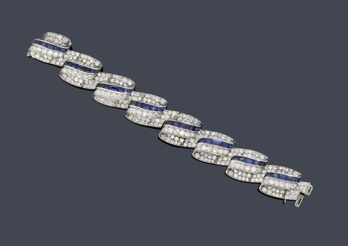 SAPPHIRE AND DIAMOND BRACELET, ca. 1950. Platinum ca. 600, 61g. Very fancy bracelet, the links designed as scrolled bands set with baguette-cut sapphires weighing ca. 6.70 ct and set throughout with 392 brilliant-cut diamonds weighing ca. 27.00 ct. W ca. 2 cm, L ca. 17.5 cm. With case.