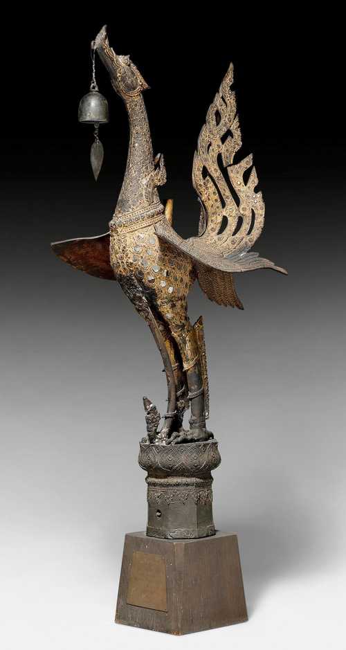 A BRONZE FIGURE OF A MYTHICAL BIRD WITH GILDING AND MIRRORED GLASS APPLIQUÉS, CLASPING A BELL PENDANT IN ITS BEAK.
