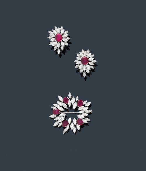 RUBY AND DIAMOND EAR CLIPS WITH BROOCH, GÜBELIN, ca. 1960. White gold 750. Classic-elegant ear clips designed as stylized blossoms, each set with 1 fine, oval ruby, weighing ca. 2.30 ct in total, each within a border of 21 navette-cut diamonds, weighing ca. 5.30 ct in total. Matching round brooch set with 5 rubies weighing ca. 4.40 ct and 34 navette-cut diamonds weighing ca. 5.80 ct. Ca. 3.6 cm Ø.