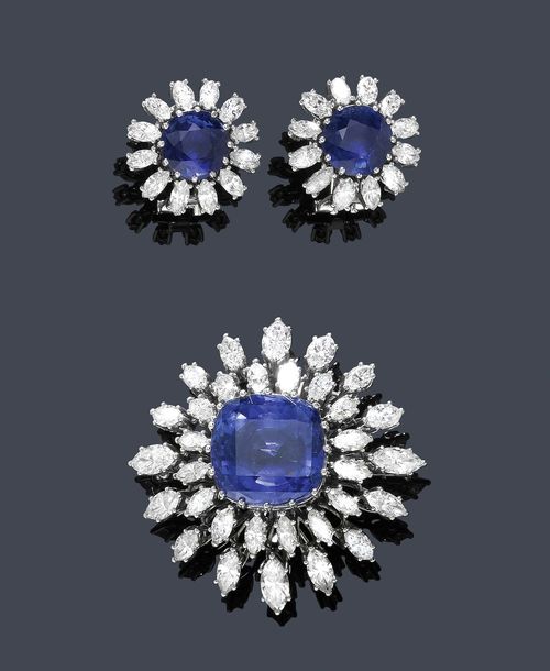 SAPPHIRE AND DIAMOND BROOCH WITH EAR PENDANTS, PAUL GERHARD HARTKOPF, ca. 1960. White gold 750. Fancy round brooch designed as a flower, set with 1 antique-oval sapphire of ca. 13.00 ct, within a border of 36 navette-cut diamonds of different sizes and weighing ca. 4.00 ct. Matching ear clips with studs, each set with 1 round sapphire within a border of 12 navette-cut diamonds. Total weight of the sapphires ca. 6.00 ct,  total weight of the diamonds ca. 1.60 ct. Matches the following lot.