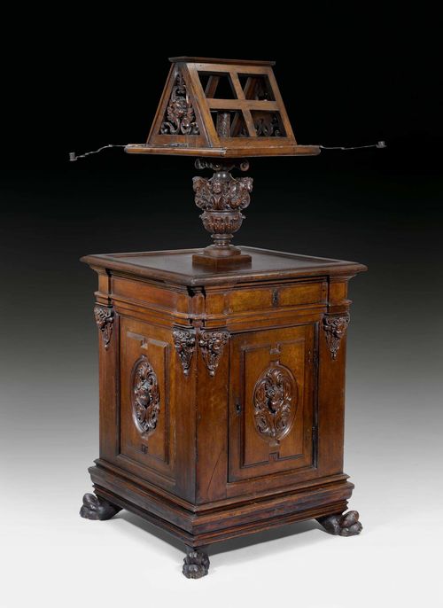 LECTERN "AUX ANGELOTS",known as a "leggio", Late Renaissance, Tuscany, 17th century. Carved walnut. Square structure with drawer above door. 2 swivelling iron candleholders. Some supplements. 87x87x198 cm.