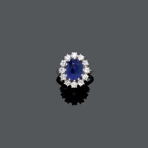 SAPPHIRE AND DIAMOND RING, ca. 1950. Platinum 900. Classic-elegant Entourage ring, the top set with 1 oval Ceylon sapphire weighing ca. 6.50 ct, unheated, slight signs of wear, within a border of 12 brilliant-cut diamonds weighing ca. 1.20 ct in total. Size ca. 54. Oral short report by GGTL/Gemlab.