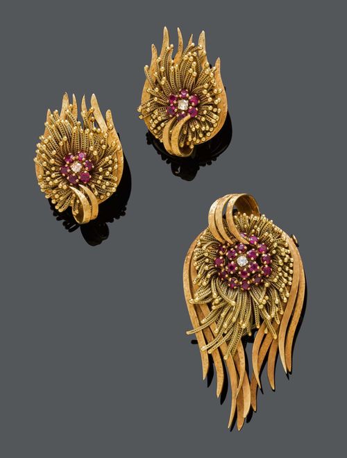 RUBY, DIAMOND AND GOLD BROOCH / PENDANT WITH EAR CLIPS, ca. 1950. Yellow gold ca. 690, 62g. Very decorative, finely satin-finished pendant designed as a stylised blossom, the centre set with 18 rubies weighing ca. 0.90 ct and 1 brilliant-cut diamond weighing ca. 0.05 ct, within a border of numerous, flexible chain parts. Matching ear clips, each with 6 rubies, weighing ca. 0.60 ct in total, and 1 brilliant-cut diamond, weighing ca. 0.10 ct in total. L ca. 6.5 and 3.5 cm, respectively.