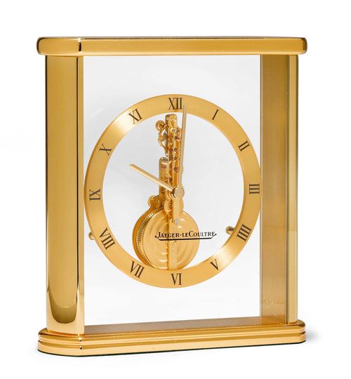 TABLE CLOCK WITH BAR MOVEMENT, JAEGER LECOULTRE, ca. 1980. Brass. Ref. 215.023. Rectangular, glass-covered brass case with visible, vertical frame, 8-day movement. Dial ring with Roman numerals and baton hands. The glass signed Jaeger Lecoultre. Movement No. 2110, Cal. 250. Ca. 13.5 x 12.5 x 4 cm.