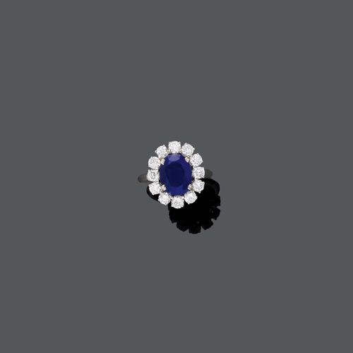 SAPPHIRE AND DIAMOND RING, ca. 1960. White gold 750. Classic-elegant ring, set with 1 oval sapphire weighing ca. 4.00 ct, unheated, within a border of 12 brilliant-cut diamonds weighing ca. 1.20 ct. Size ca. 54. Oral estimate by GGTL/Gemlab.