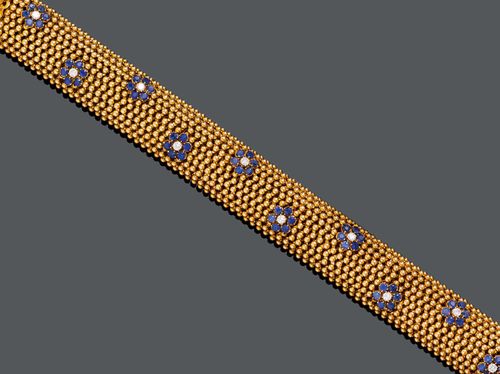 GOLD, SAPPHIRE AND DIAMOND BRACELET, ca. 1950. Yellow gold 750, 108g. Decorative, flexible, slightly convex snake bracelet decorated with spheres and additionally decorated with 10 applied rosette motifs, each with 6 sapphires and 1 brilliant-cut diamond. Total weight of the sapphires ca. 2.40 ct and total weight of the diamonds ca. 0.50 ct. W ca. 1.9 cm, L ca. 20 cm.