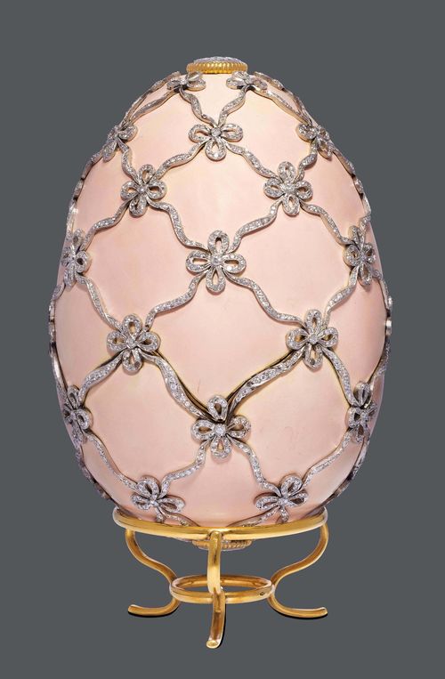 ENAMEL AND DIAMOND EGG WITH STAND, E. MEISTER. Platinum, 106g, fine gold 999, 99g and silver. Very decorative egg in the style of ca. 1910, matte-enamelled on all sides in shades of antique pink, and decorated with applied band and bow motifs set throughout with numerous brilliant-cut diamonds weighing 13.61 ct. Ca. 11 x 7.5 cm. Stand in yellow gold 750. With case.