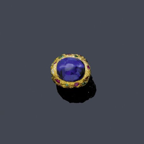 TANZANITE, GEMSTONE AND DIAMOND RING. Yellow gold 750. Casual-elegant mantle ring with a textured surface, the top set with 1 fine, blue oval tanzanite cabochon of ca. 28.00 ct decorated with 10 tourmalines, 8 rubies, 2 sapphires, 2 peridots, 2 citrines, 1 emerald and 1 brilliant-cut diamond weighing ca. 4.00 ct. Size ca. 50. With report by Walter Grün, October 2003.