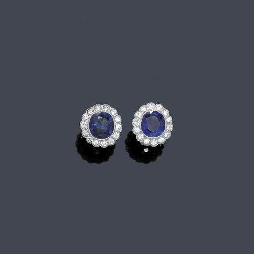 BURMA SAPPHIRE AND DIAMOND EAR STUDS. Platinum. Classic-elegant ear studs, set with 1 oval, unheated Burma sapphire of 1.62 ct and 1.52 ct, respectively. Each within a border of 14 brilliant-cut diamonds, total weight of the diamonds ca. 0.80 ct. With GPL Reports Nos. 2239 and 2240 of 17 November 2009.