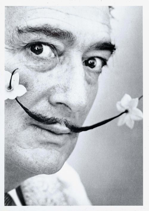 Halsman, Philippe (1906-1979). Salvador Dalí mit blumenbestücktem Schnurrbart. Silbergelatineabzug. Vintage. [1954]. 18 x 12,4 cm. Rückseitig mit Photographenstempel.