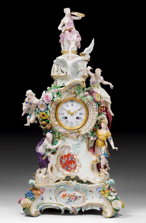 LARGE IMPORTANT CLOCK WITH THE POLISH ROYAL COAT OF ARMS AND ALLEGORICAL FIGURES, Meissen,19th century. The model by by J.J.Kändler and  J.F. Eberlein from 1743. Modelled with rocaille heightened in turquoise and pink, with applied flowers and flanked by allegorical figures and putti, crowned by the Polish eagle. Set on a later plinth with rocaille feet and applied flowers. The clock with Paris movement striking the 1/2 hours on bell. Underglaze blue sword marks, model number incised 452. The clock H 60cm, the plinth H 11cm. Minor restoration.(2)