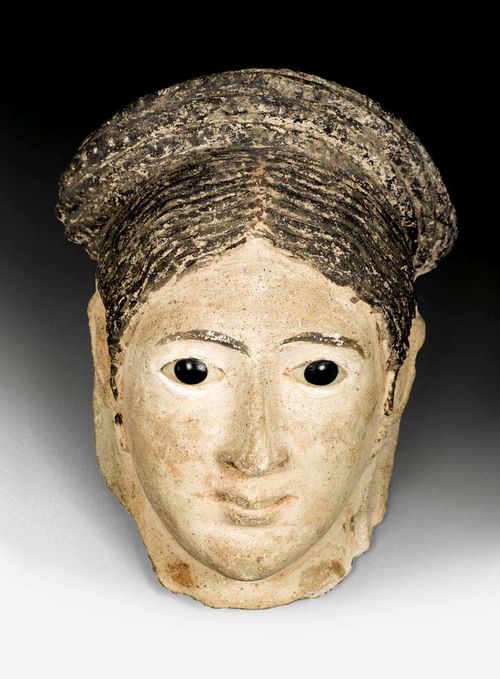 EGYPTIAN-STYLE PAINTED MASK OF A YOUNG WOMAN,probably circa 1900. Polychrome painted clay. With glass eyes. Somewhat chipped. H 26 cm. Provenance: from an important German private collection.