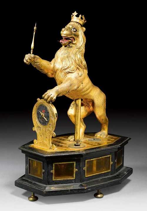 TABLE CLOCK WITH LION AUTOMATON,Renaissance, Augsburg, 17th century Matte and polished gilt bronze and ebonised wood. The lion with sceptre and crown, also moveable eyes and muzzle. The clock with 2 small dials, enamel dial with Roman numerals and verge escapement with striking mechanism. Requires restoration. 21x12x35 cm. Provenance: from an important German private collection. The pair to this piece is in the Württembergisches Landesmuseum in Stuttgart and illustrated in: R. Mühe / H.M. Vogel, Alte Uhren, Munich 1976; p. 57, ill. 21.