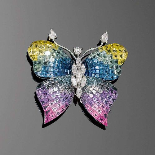 SAPPHIRE AND DIAMOND BROOCH. White gold 750. Fancy brooch in the shape of a butterfly, the wings entirely set with numerous carré-cut sapphires in rainbow colours, totalling ca. 35.80 ct, invisible setting, the body set with 8 navette-cut diamonds, the head set with 1 brilliant-cut diamond, the feelers set with 2 drop-shaped diamonds. Total diamond weight: ca. 1.22 ct.