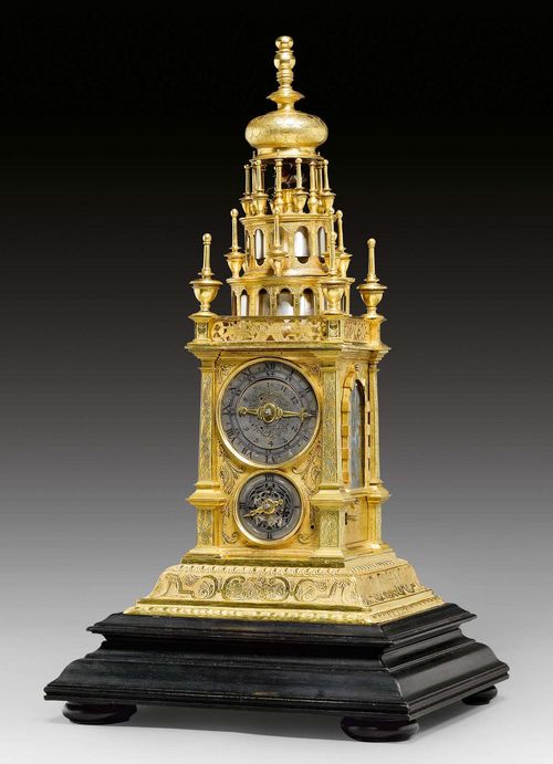 TURRET CLOCK,Renaissance, Augsburg circa 1600. Gilt brass, exceptionally finely engraved on all sides. On a later pivoting base. The front with silver dial, engraved with Roman and Arabic numerals for hours and minutes, above a smaller dial with Roman numerals for the quarter hours. Alarm disc verso. Partly glassed sides. Fine verge escapement with striking on 2 bells. 15x15x35.5 cm. With base 23x23x42 cm.