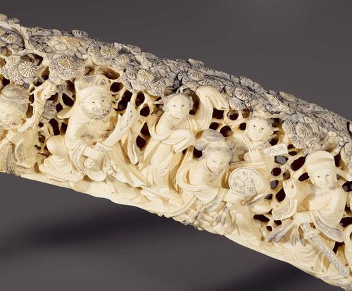 MONUMENTAL ELEPHANT TUSK.China, late Qing Dynasty, L 156 cm. Elaborate carving of a congregation of deities in a pine forest, borne by a cloud cover. The forest is lightly blackened. Wooden stand.