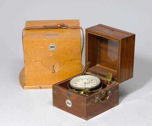 SHIP CHRONOMETER, Ulysse Nardin, No. 5058, ca. 1944. Cylindrical brass case mounted in a square mahogany box. With 2 hinged covers, the second cover with a glass. Seconds and power reserve. Handles for carrying on the side (19x19x19 cm). In an additional wooden box enclosed with leather straps.