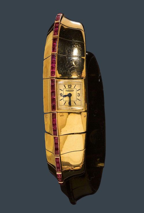 RUBY AND GOLD LADY'S WRISTWATCH, JAEGER, ca. 1937. Yellow gold 750. Rare, asymmetrical bracelet with ruby-set border and integrated watch. 73 synthetic square-cut rubies in total. Rectangular, asymmetrical case No. 81601 with convex glass, crown on the back. Gold-coloured dial signed Jaeger, with black indices and numerals and blue-Breguet hands. Hand winder, movement No. 100815, Cal. 10 signed. French import Marks. L ca. 18 cm. With case, not original.