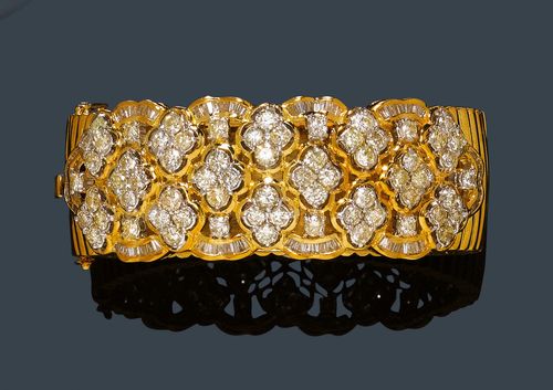 DIAMOND AND GOLD BANGLE. Yellow gold 750, 86g. Decorative, broad, gadrooned bangle, the floral open-worked top decorated with 14 rosette and band motifs set with brilliant-cut diamonds and baguette-cut diamonds. Total weight of the baguette-cut diamonds ca. 1.00 ct and of the 66 brilliant-cut diamonds ca. 6.10 ct. W ca. 2.2 cm, ca. 6 x 5 cm.