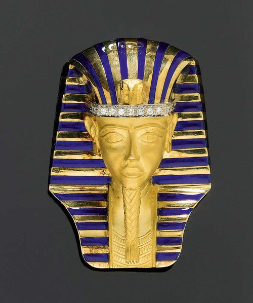 GOLD, ENAMEL AND BRILLIANT-CUT DIAMOND BROOCH, ENRICO SERAFINI, Florence, 1960s. Yellow gold 750, 99g. Large, decorative brooch in the shape of a gold death mask of Tutankhamen with the typical Nemes head scarf in gold with a blue enamelled stripe pattern. The headband is decorated with a row of 11 brilliant-cut diamonds totalling ca. 0.50 ct. Face, beard and chest in fine matte-polished gold. The back decorated with fine volute motifs and two Egyptian ladies making music. Unsigned. 7.5 x 5.4 x 3 cm. Enrico Serafini (1913-1968) was an esteemed artist and goldsmith. Most of his work is unsigned. From the collection of a castle in West Switzerland. Directly acquired from the artist.