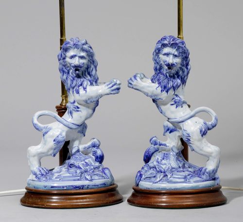 PAIR OF TABLE LAMPS WITH LION FIGURES, France, ca. 1880. Faience, brass and wood. Rearing lion. Base with coat-of-arms and inscribed "St. Clement". On a wooden plinth with brass arm for the candle holder. H 66.5 cm. Provenance: Gut Aabach, Risch am Zugersee.